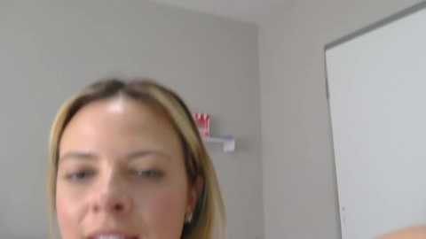 A blurry video of a blonde woman with fair skin and light makeup, likely taken indoors, showing a close-up of her face and upper body.