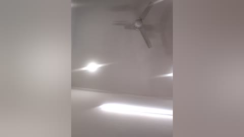 Video of a ceiling with a modern, white ceiling fan and a bright, circular light fixture. The walls are painted in a soft, neutral shade, creating a minimalist, clean atmosphere.