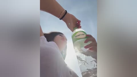 A video captures a young woman with light skin and long brown hair, wearing a green shirt, drinking from a clear water bottle. A woman with a tan wrist and red nails pours water from a green bottle.