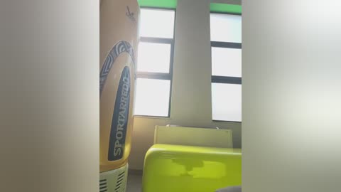 Video of a beige spray can with \"SPRAYZET\" label, partially blocking a window with frosted glass. Green and yellow plastic chairs are visible in the background, suggesting a clean, modern, and well-lit indoor setting.