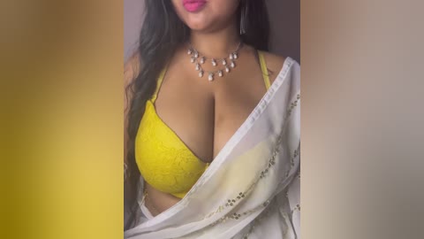 Video of a South Asian woman with medium-dark skin, wearing a yellow lace bra and a white sari, adorned with a pearl necklace.