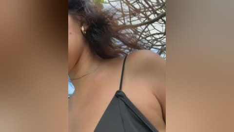 Video of a woman with medium brown skin, wearing a black halter top, kissing a man with light skin, both outdoors against a blurred background of tree branches.