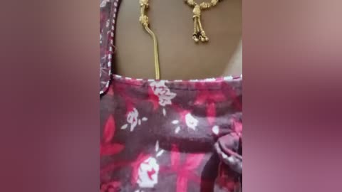 A close-up video of a woman's upper torso wearing a floral dress with red and white roses, paired with gold dangling earrings. The background is blurred.