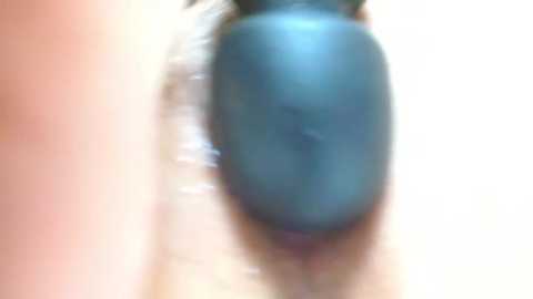 A close-up video of a person's hand applying a large, round, teal-colored object to their face, possibly a mask or large bandage. The background is blurred and out of focus, emphasizing the action.