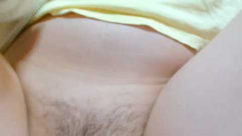 A close-up video of a woman's lower abdomen and pubic area, showing natural, light brown pubic hair and a light yellow fabric partially covering the area. The image is explicit and focuses on the intimate details.