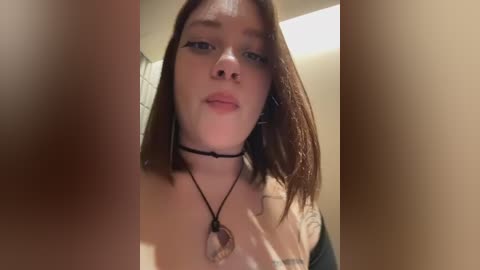A video of a young woman with shoulder-length brown hair, wearing a black choker necklace, and a black top, standing in a dimly lit bathroom.