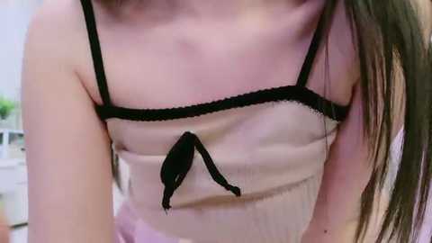 Video of a fair-skinned woman with long brown hair, wearing a sheer beige camisole with black lace trim and a small bow, seen from the neck down.