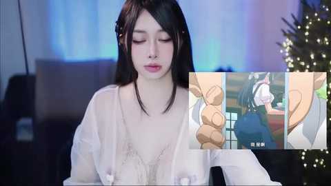 Video of an Asian woman with long black hair and fair skin, wearing a sheer white dress, in a cozy, dimly lit room with a Christmas tree and presents.