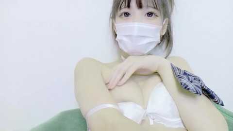 A young Asian woman with fair skin, wearing a white face mask, a white bra, and a blue-and-white-patterned scarf, poses indoors against a plain white background.