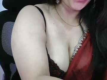 Video of a light-skinned woman with dark hair, wearing a black lace bra and red shawl, seated in a car.