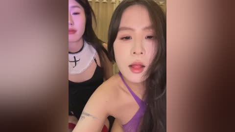 Video of two young Asian women, one with long black hair, wearing a purple top, and the other with straight dark hair in a black tank top, both smiling.