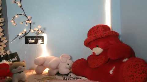 A video of a cozy, child's room with a red teddy bear in a crocheted hat, a white bear, and a soft light on the wall.