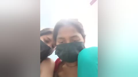 Video of two women in a dimly lit room, one with a black mask and the other partially visible.