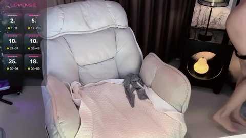 Video of a plush, white leather recliner with a stuffed toy on a pink blanket. The background features dark curtains and a lit lamp.