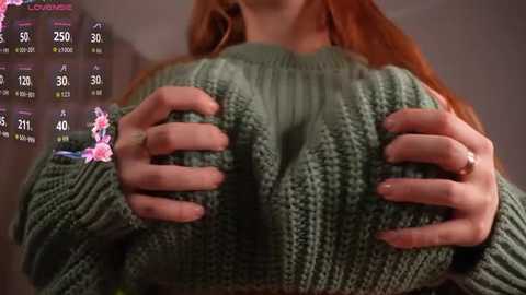 Video of a woman with long, red hair wearing a green, knitted sweater. She holds her large breasts with both hands, showing cleavage. Weather forecast overlay in the background.
