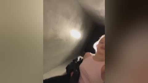 Video: A close-up of a person lying on their side, partially obscured by a black object. The person wears a pink tank top, and their face is partially visible. The background is dimly lit.