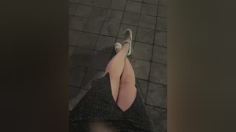 A video showing a woman's legs and feet in white sneakers and black patterned shorts, sitting on a tiled floor. The background is dimly lit, creating a moody, intimate atmosphere.