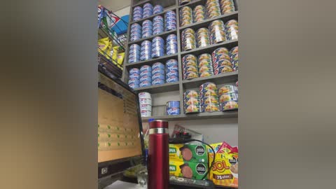 Video of a small, neatly organized pantry. Rows of canned goods and snacks fill shelves, including Campbell's soup and boxes of cereal. A red water bottle sits in the foreground.