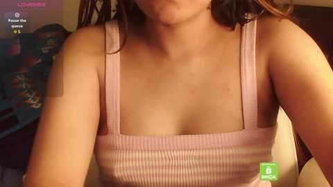 Media: Video of a young woman with light skin, wearing a pink striped tank top, her face partially visible, in a casual indoor setting.