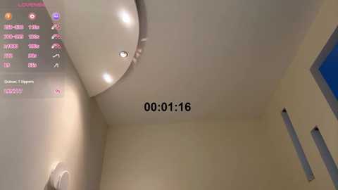 A video of a modern, minimalist room with a white ceiling featuring a round, recessed light fixture. The room has beige walls, and a digital clock displays \"00:01:16.\" The setting appears clean and uncluttered.