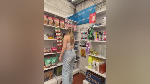 Video of a supermarket aisle with a woman in a white tank top and blue jeans browsing shelves, stocked with snacks, cleaning products, and household items.