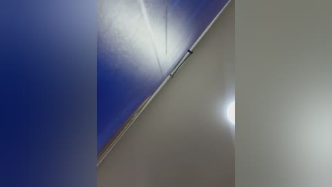 Video of a modern interior corner with a blue sky peeking through a rectangular window, creating a striking contrast. The room's walls are white, and the sunlight casts a bright reflection, adding depth and a sense of openness.