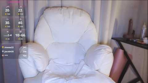 A video of a white, cushioned armchair against a beige curtain backdrop. The image is overlaid with social media video statistics and icons.