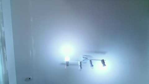 A video showing a dimly lit, foggy bathroom with a chrome light fixture emitting a bright white light, casting a soft glow on the white walls. The image is slightly blurred, adding a mysterious, dreamlike quality.