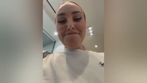 A video captures a young woman with fair skin, wearing a white T-shirt, and closed eyes, partially obscured by the frame. The background features modern, minimalist interior elements.