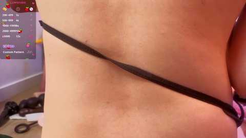 A close-up video of a light-skinned person wearing black lingerie, showcasing the side profile of their torso. Background features a gaming interface with colorful icons.