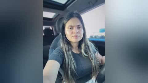Video of a Latina woman with long, straight, dark hair and medium skin tone, wearing a gray t-shirt, seated in a car.