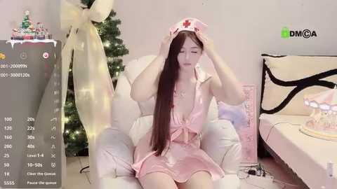 A video of a young woman in a pink nurse outfit, adjusting her headband, in a cozy, Christmas-decorated room.