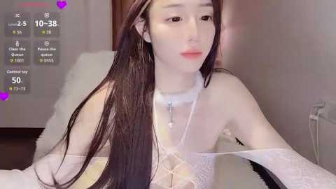 Video of a pale-skinned, slender Asian woman with long black hair, wearing a sheer white lace dress and a choker, sitting indoors.
