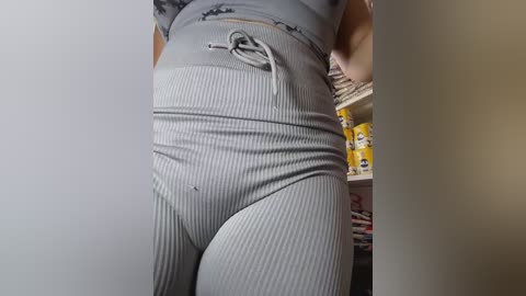 Media: Video of a person wearing tight, grey ribbed leggings, showcasing their toned legs and buttocks. The background reveals a cluttered kitchen with yellow containers and a woven basket.