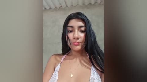 Video of a young woman with long black hair, wearing a white lace halter top, standing in a tiled room with beige walls.