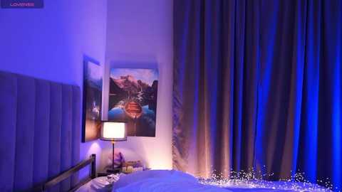 Video of a modern, dimly-lit bedroom with a white bed, grey curtains, a lamp, and a colorful landscape print on the wall, bathed in blue and purple hues.