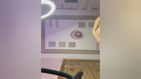 Media: Video of a ceiling with a circular, pink ceiling fan, beige rectangular panels, and wooden door with intricate patterns, under warm lighting.