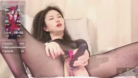 Media: A video of an Asian woman with long black hair, wearing a sheer black bodysuit, masturbating with a pink vibrator. The background shows a white curtain and bed.