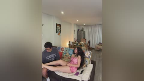 Media: A video of a man and woman, dressed casually, sitting on a colorful sofa in a modern, well-lit living room with white walls and beige flooring.