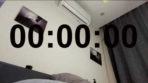 Video of a minimalist bedroom with white walls, an air conditioner, two black-and-white framed photos, and a bed with gray pillows. Text \"00:00:00\" overlays the center, emphasizing the room's timelessness.
