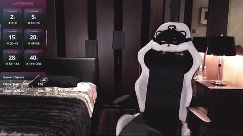 Video of a gamer in a black gaming chair, wearing a VR headset, in a dimly lit bedroom with a bed, nightstand, and lamp.