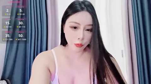 A video of a fair-skinned, long-haired East Asian woman in a pink spaghetti-strap top, with a video feed overlay showing viewers' numbers.