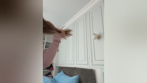 Media: A video of a woman combing her long, light brown hair in a modern bedroom with white-paneled walls, a gray headboard, and a light blue pillow.