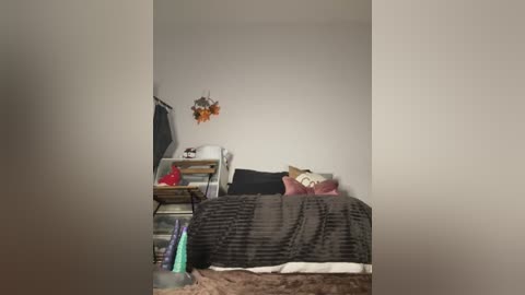 A video of a small, cluttered bedroom with a beige wall, a messy bed with a striped gray comforter, and a wooden nightstand.