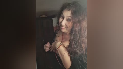 Video of a smiling woman with curly brown hair, wearing a black top, holding a camera. She has fair skin and is indoors with a blurred background.