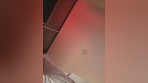 Video of a close-up view of a woman's chest, featuring a small, circular nipple piercing, with a reddish hue in the background.