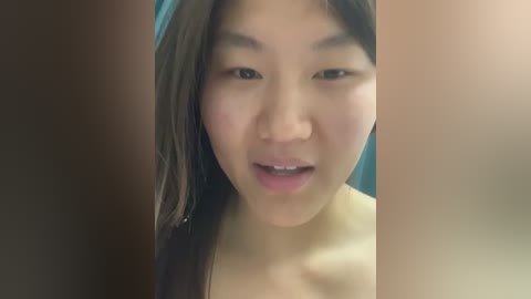 Media: Video of a young Asian woman with straight, dark brown hair and light skin, wearing a strapless top, looking directly at the camera with a slight smile.