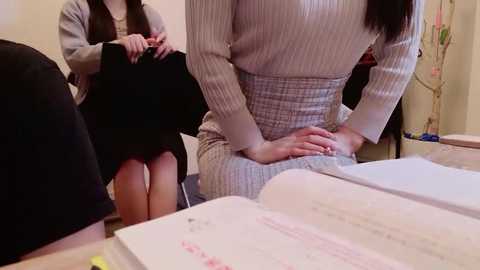 Media: Video of a woman in a pinstriped suit teaching two women seated at a table with open books, one wearing a black dress, the other a gray sweater.