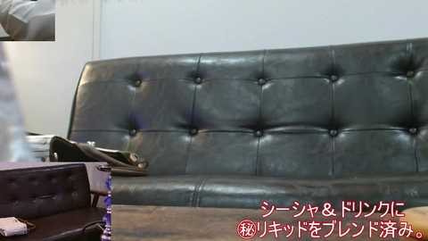Video of a dimly lit room with a dark green, tufted leather sofa against a white wall. A person, blurred, stands near the sofa. Japanese text in red and white is visible in the bottom right corner.