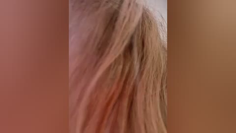A close-up video of a person's shoulder and neck, with long, straight, light brown hair flowing over the shoulder. The background is blurred and monochromatic, emphasizing the texture and movement of the hair.